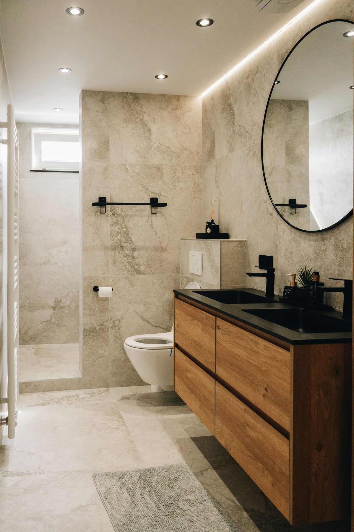 Marble-tiled walk-in shower with matte black fixtures and a round mirror, designed by Basalt & Birch
